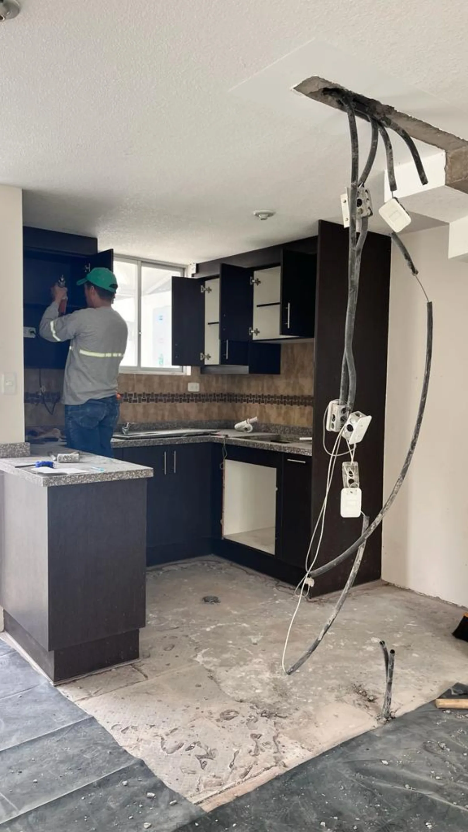 Cocina antes de la remodelación con gabinetes antiguos, piso retirado e instalaciones expuestas