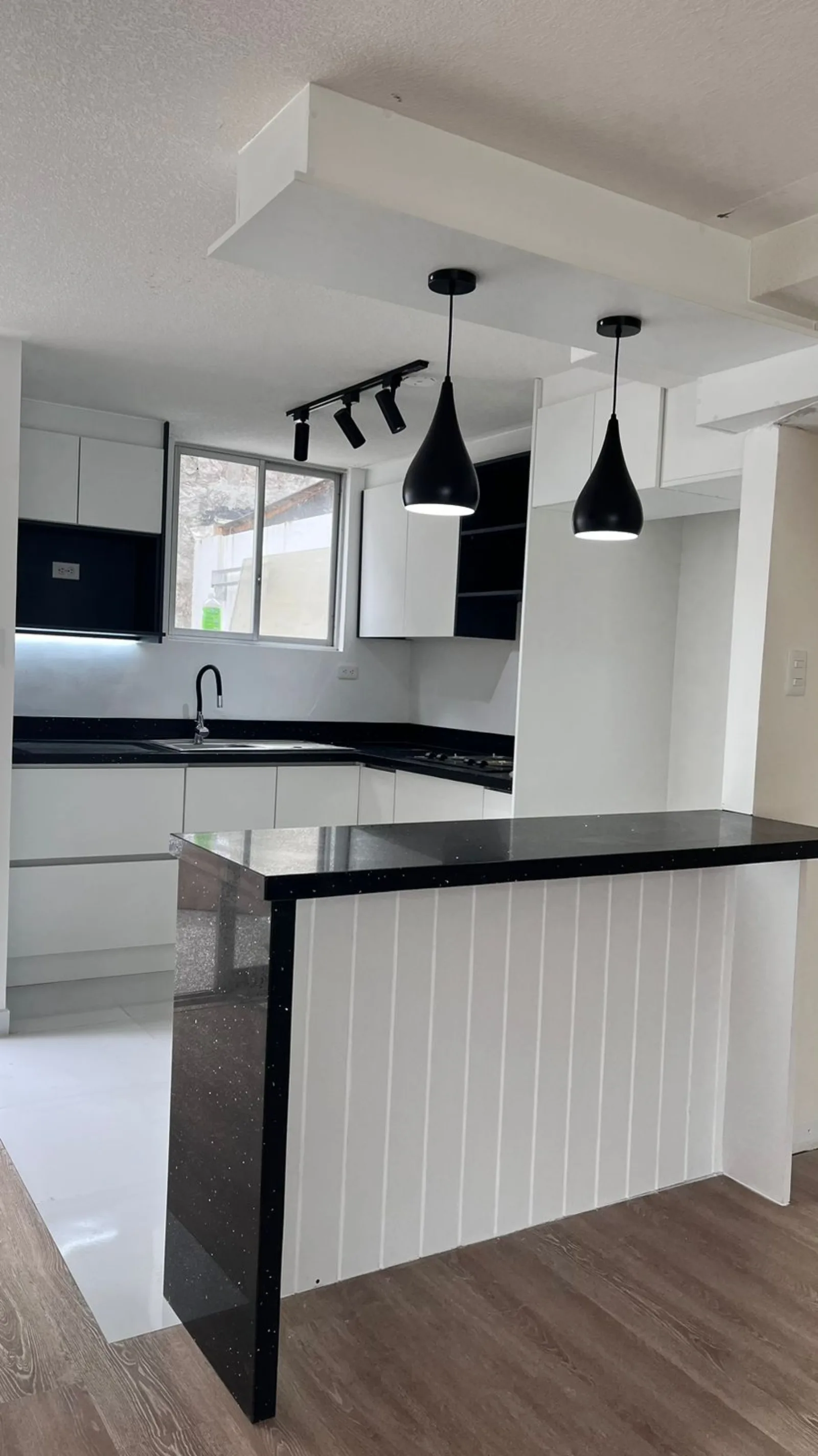 Cocina terminada con gabinetes blancos, mesón negro, piso nuevo e iluminación instalada