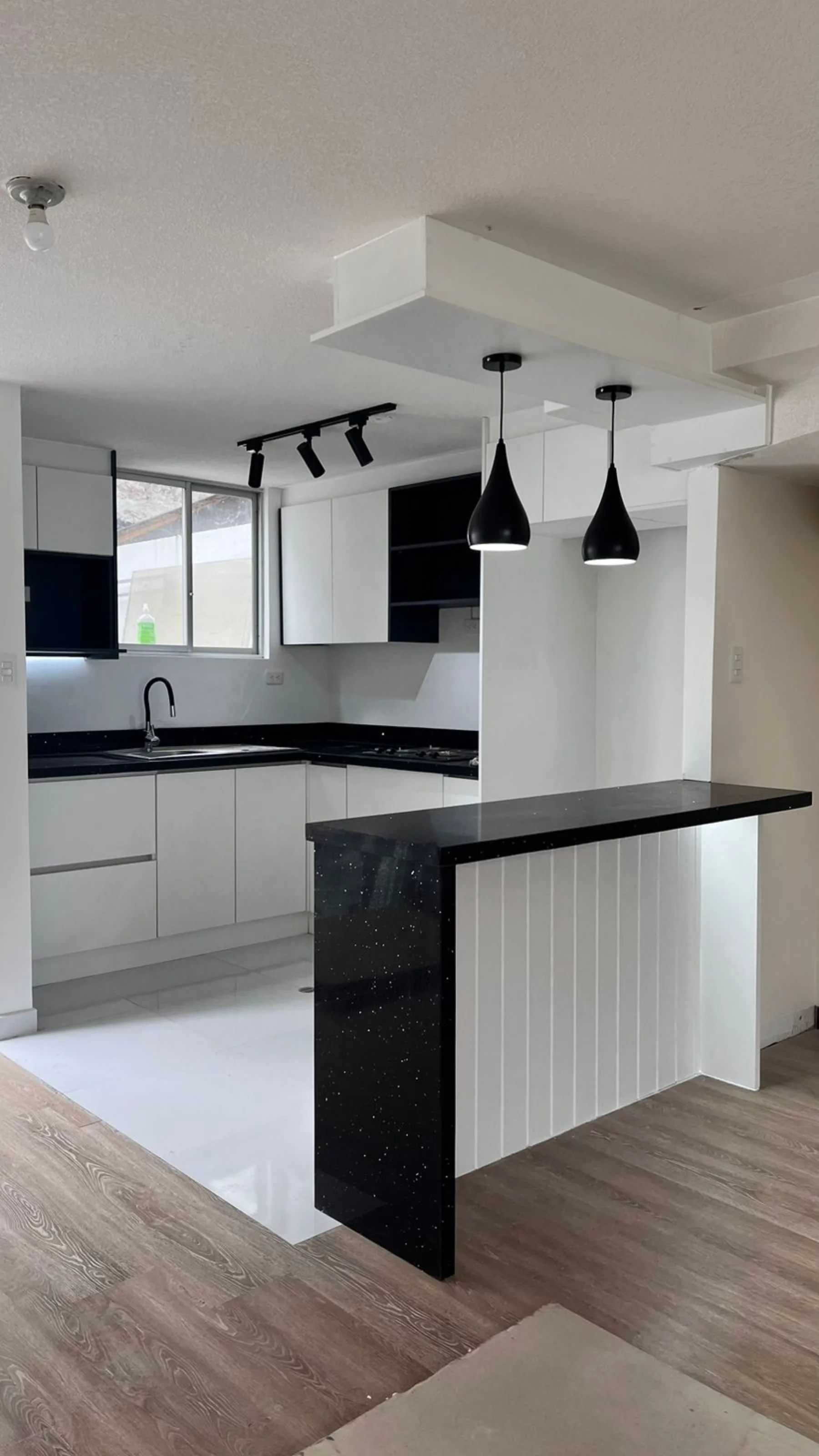 Cocina residencial remodelada en Quito con mesón negro, gabinetes blancos e iluminación colgante