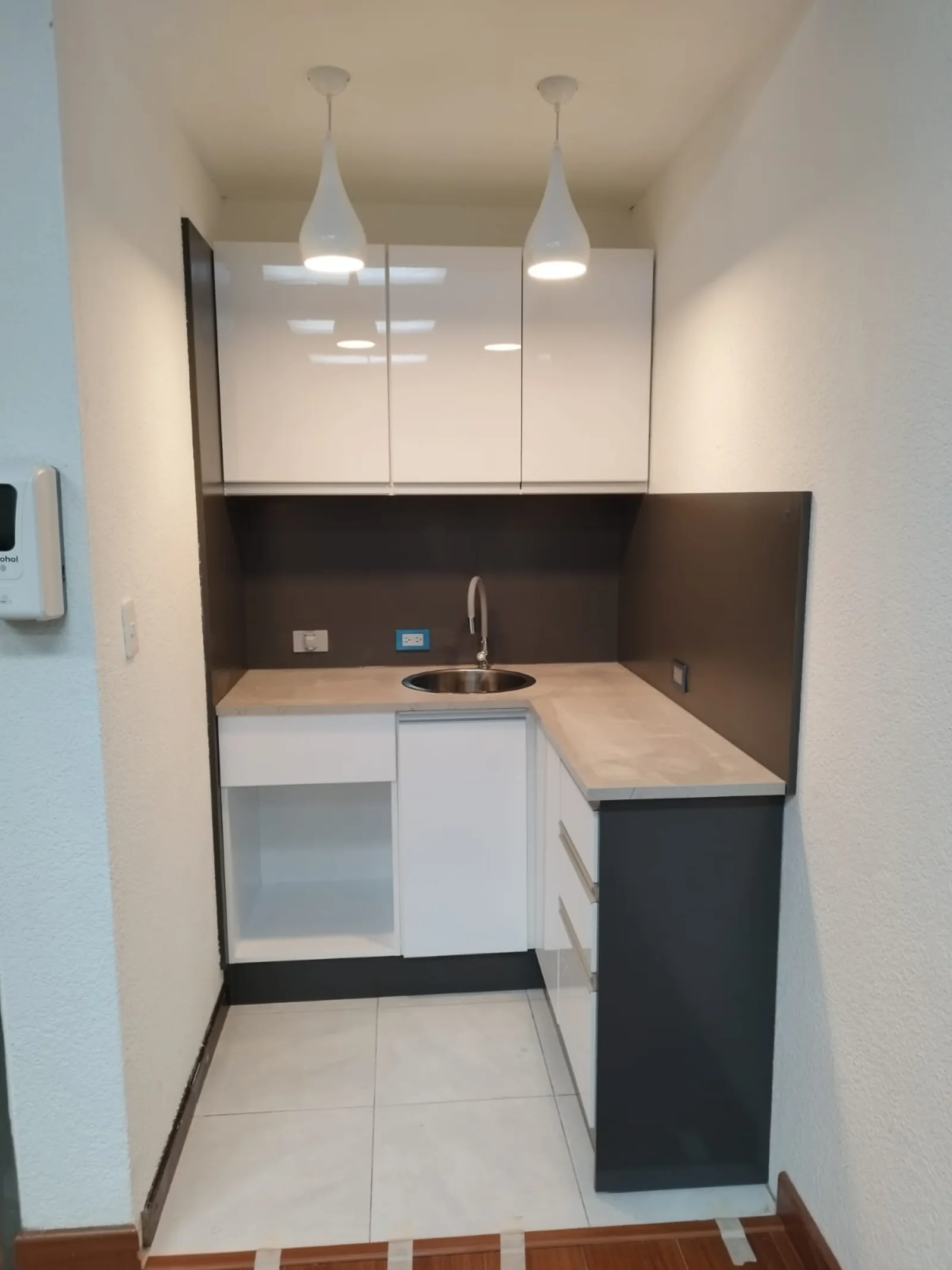 Kitchenette corporativa con muebles altos y bajos, lámparas colgantes y fregadero